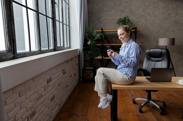 Successful young businesswoman hold phone and sitting on desk