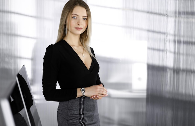 Successful young businesswoman is standing straight in a\
cabinet of a firm. business headshot or portrait of a secretary in\
an office