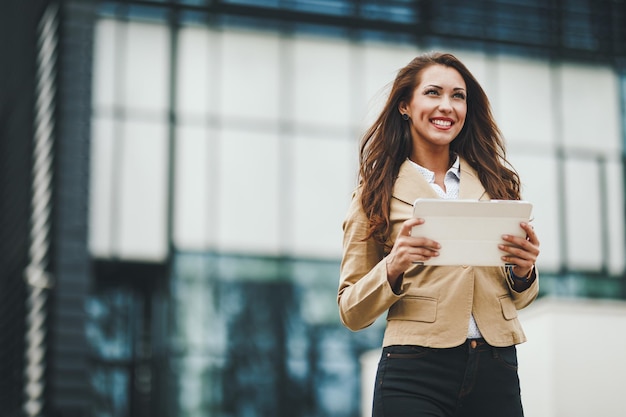 Successful young businesswoman working on digital tablet in\
front of office district.