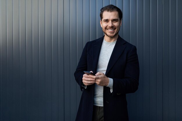 Successful young software engineer with a wide smile on his face and a mobile phone in his hands