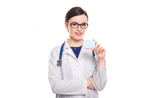 Successful young woman doctor with stethoscope with arms crossed showing business card in white uniform