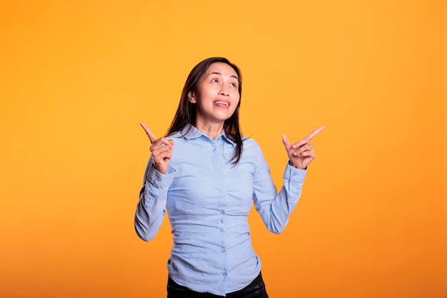 Succesvol Filipijns model wijzende vinger omhoog poseren in studio op gele achtergrond. Zelfverzekerde positieve vrouw die reclame maakt voor een verkoopproduct, met een advertentiepictogram of voorbeeld op de camera. Advertentie-concept