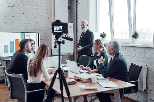 Succesvol zakenteam luistert naar een man die een presentatie geeft tijdens het filmen van een personeelsvergadering in de bestuurskamer