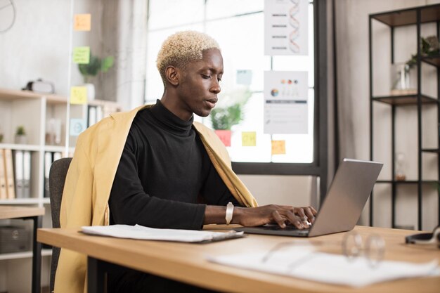 Succesvolle Afrikaanse zakenman in stijlvol pak werken op laptopcomputer op moderne kantoor