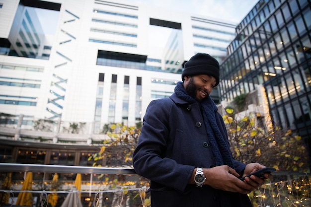 Succesvolle Afro-Amerikaanse zakenman controleert de meldingen op zijn smartphone, het is winter, het is koud en hij is buiten