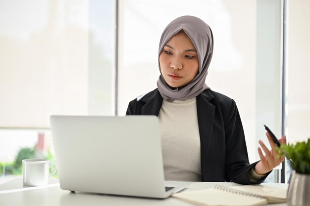 Succesvolle Aziatische moslimzakenvrouw die laptop gebruikt en zich concentreert op haar taken op kantoor