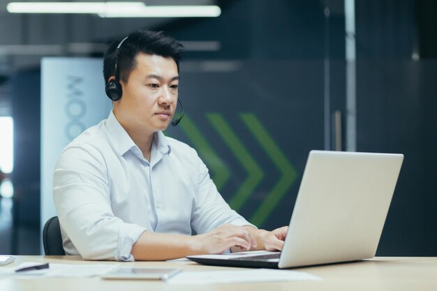 Succesvolle Aziatische werknemer baas zakenman werken met laptop met behulp van headset voor video-oproep man bij