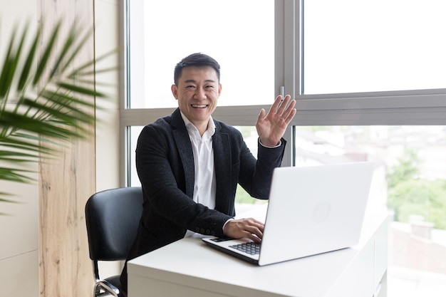 succesvolle aziatische zakenman in een zwart pak werkt op een laptop in een stijlvol kantoor