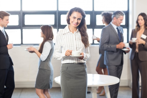 Succesvolle bedrijfsvrouw die terwijl haar collega&#39;s glimlachen die zich achter haar in bureau bevinden