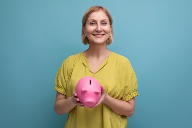 Succesvolle blonde volwassen vrouw bewaart geld in een spaarvarken en denkt waar ze het in kan investeren