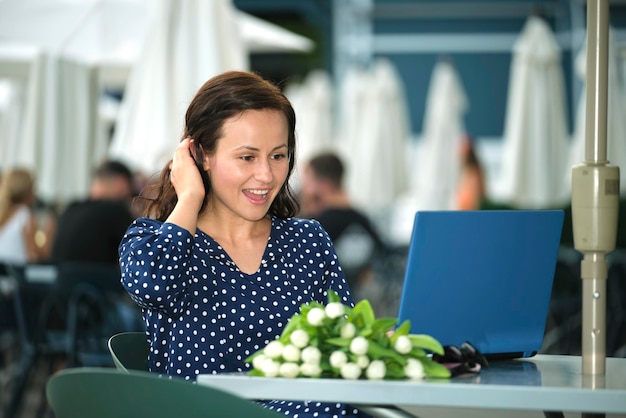 Succesvolle gelukkige vrouw die vooruitgang viert door op afstand te werken op een laptop die aan tafel zit in een openluchtcafé Concept van zaken online doen