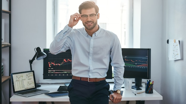 Succesvolle handelaar moderne jonge zakenman in formele kleding die zijn bril aanpast en kijkt naar