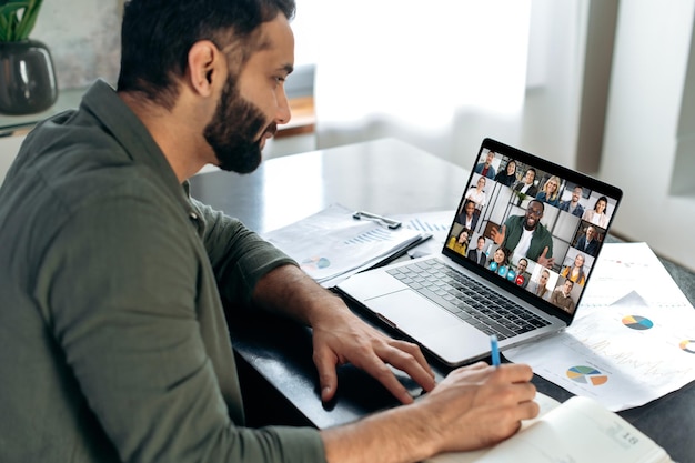 Succesvolle Indiase man met laptop voert virtuele ontmoeting met zakenpartners tijdens een videogesprek Groep diverse multiraciale zakenmensen op laptopscherm praten via videoconferentie