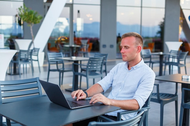 Succesvolle jonge executive kijkt terwijl hij aan een tafel zit met een laptop op een hotelterras en tijd vindt voor afstandsbediening van werknemers terwijl hij op vakantie is in een exotisch resort