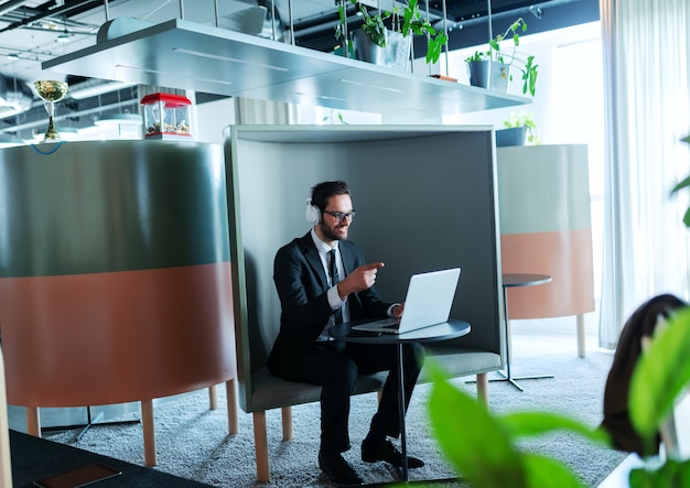 Succesvolle jonge manager die een conferentiegesprek heeft en in zijn werkstation zit. Koptelefoon op oren.