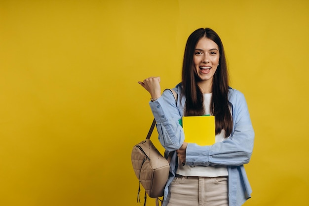 Succesvolle jonge student die boeken vasthoudt en handen schudt op gele achtergrond Het concept van leren op school en universiteit