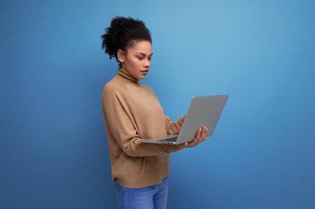 Succesvolle jonge studente met een donkere huid en pluizig haar die op afstand studeert met een laptop aan