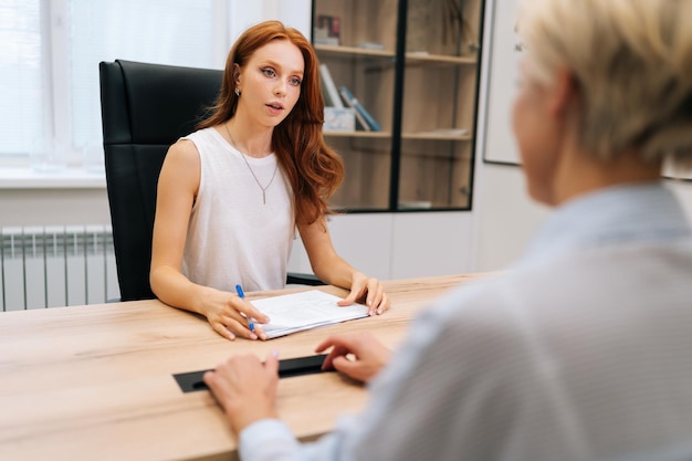 Succesvolle jonge zakelijke mentor vrouw die praat met een middelbare werknemer stagiaire op de werkplek
