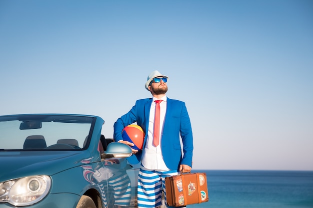 Succesvolle jonge zakenman op een strand Man die in de klassieke auto van de cabrio staat?