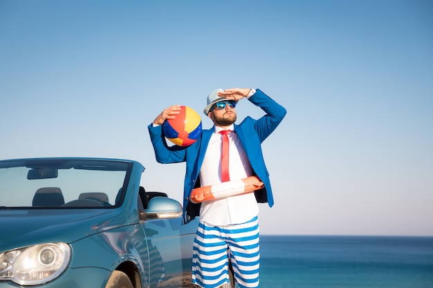 Succesvolle jonge zakenman op een strand Man die in de klassieke auto van de cabrio staat?