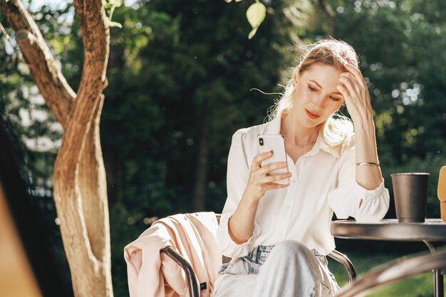 Succesvolle jonge zakenvrouw die op een terras zit en smartphone gebruikt using