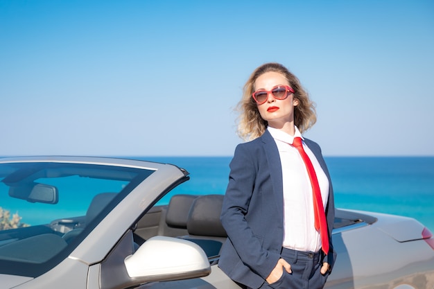 Succesvolle jonge zakenvrouw op het strand Vrouw die zich dichtbij de klassieke auto van cabriolet bevindt