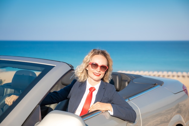 Succesvolle jonge zakenvrouw op het strand Vrouw zit in de klassieke auto van de cabrio