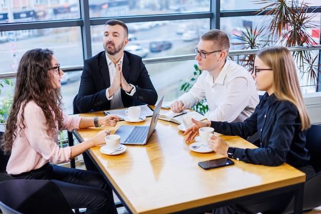 Succesvolle knappe mannelijke mentor, directeur, zakenman in een pak in een kantoor met ondergeschikten. Werkdag concept. Teammeeting met de baas op de voorgrond