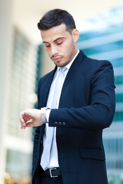 Succesvolle knappe zakenman die zijn horloge bekijkt