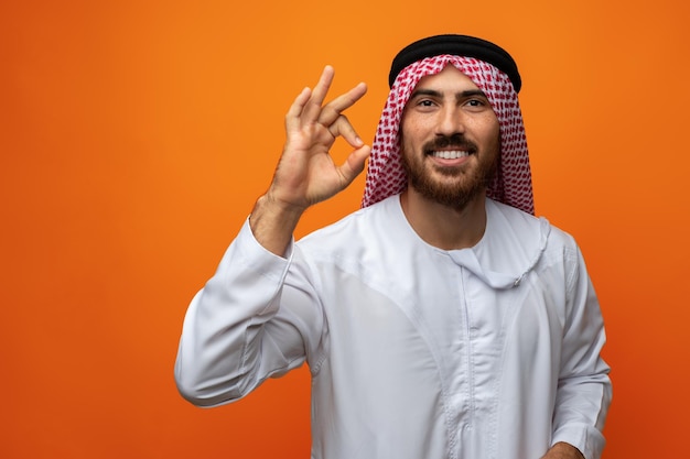 Succesvolle lachende jonge Arabische man viert overwinning op oranje achtergrond