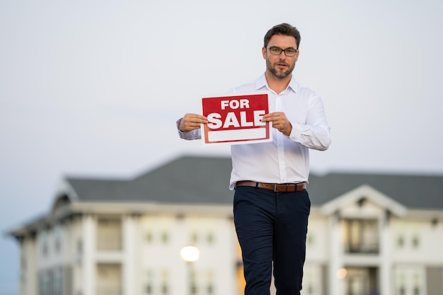 Succesvolle makelaar in onroerend goed in een pak met te koop bord in de buurt van nieuwe appartement makelaar wi