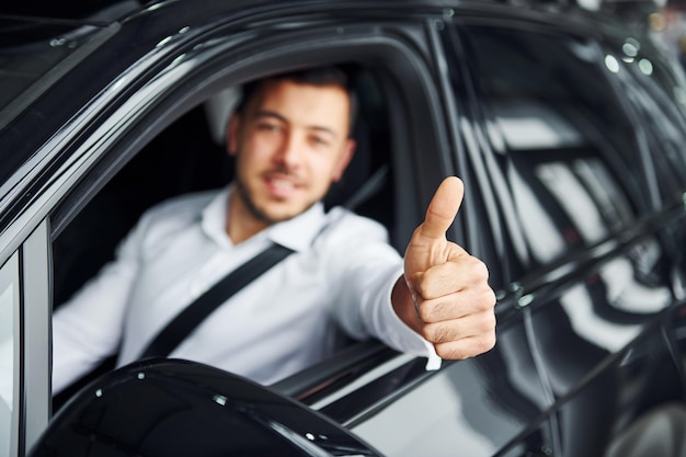 Succesvolle man Jonge man in wit overhemd zit in een moderne nieuwe auto