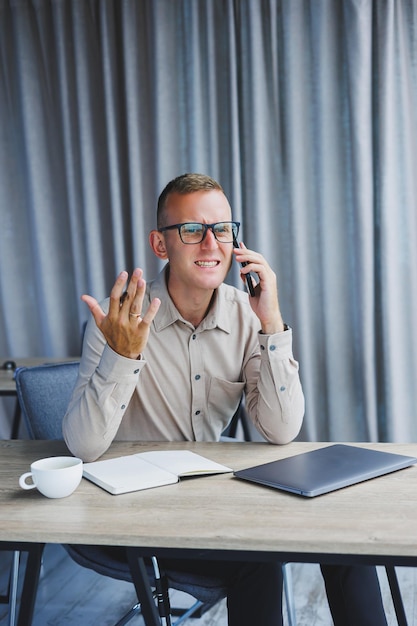 Succesvolle man praten op smartphone en browsen netbook tijdens het surfen op internet in kantoor aan tafel