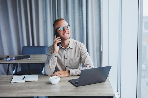 Succesvolle man praten op smartphone en browsen netbook tijdens het surfen op internet in kantoor aan tafel