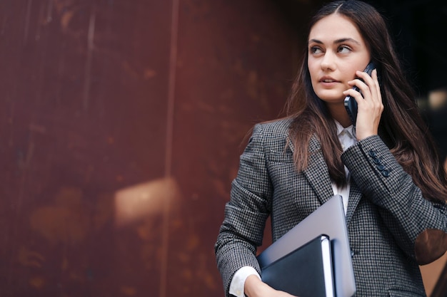 Succesvolle mooie jonge zakenvrouw praten op mobiele telefoon terwijl laptop in handen op weg naar werk Kopieer ruimte Bedrijfsfinanciën concept Zakenvrouw praten over een werkproject