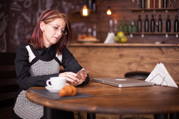 Succesvolle onderneemster die haar telefoon naast Franse croissant controleert. Gezellig vintage restaurant