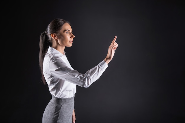 Succesvolle onderneemster. Slimme serieuze jonge vrouw die voor het sensorische scherm staat en ernaar kijkt terwijl ze zich op haar werk concentreert