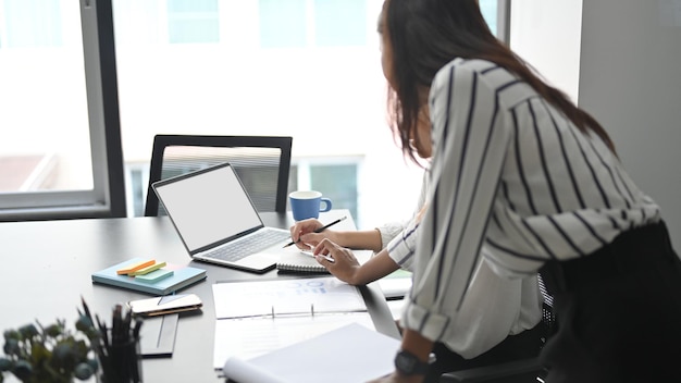 Succesvolle professionele zakenvrouwen die samen op kantoor online ideeën voor hun zakelijk project doornemen. laptop leeg scherm mockup.