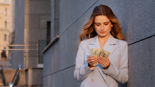 Succesvolle rijke kaukasische duizendjarige zakenvrouw die in de buitenlucht op straat staat en geld aan het tellen is met dollars bankbiljetten rekening budget telling salaris smeergeld na te denken over financiën betalingen rijkdom