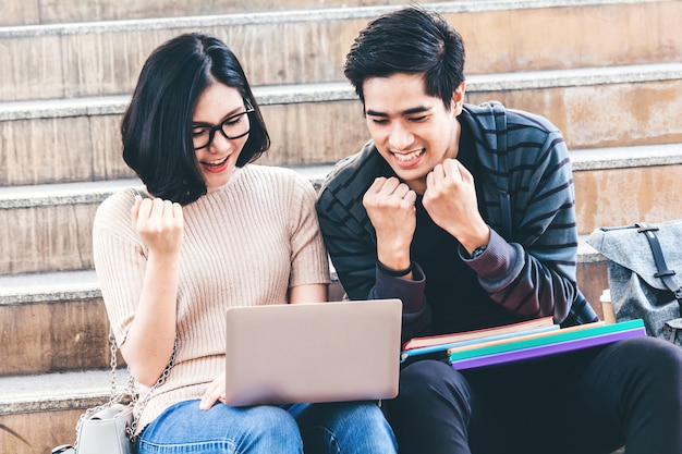 Succesvolle studenten vieren met armen omhoog en huiswerk met boeken en laptop