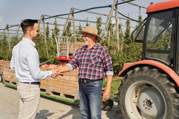 Succesvolle transactie tussen senior boer en verkoopvertegenwoordiger op een appelboomgaard