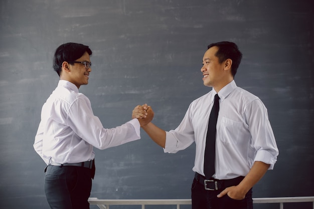 Succesvolle twee Aziatische zakenman in overhemd en stropdas die lacht terwijl hij teamhanddruk doet
