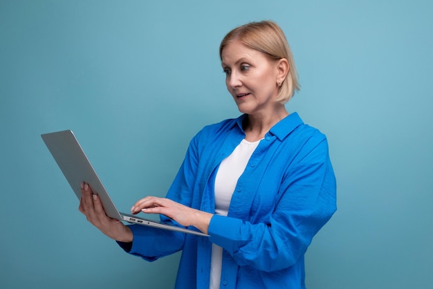 Succesvolle volwassen zakenvrouw die op afstand werkt met behulp van laptop op blauwe achtergrond met kopieerruimte