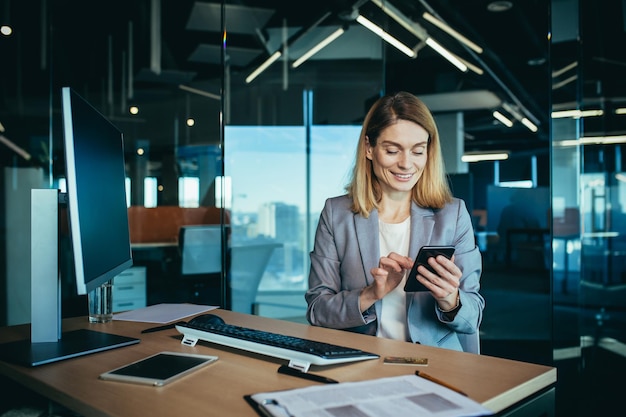 Succesvolle vrouw die in een modern kantoor aan een computer werkt zakenvrouw gebruikt de telefoon sociale netwerken online browsen