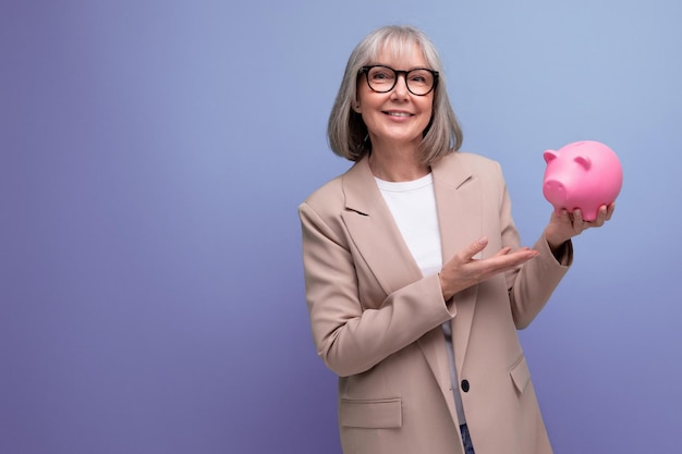 Succesvolle vrouw van middelbare leeftijd met een spaarvarken op een lichte achtergrond met kopieerruimte