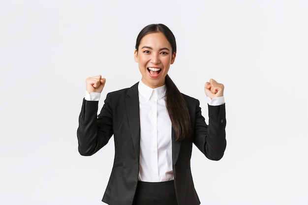 Succesvolle winnende vrouwelijke ondernemer in zwart pak, vuistpomp en ja opgewonden schreeuwend, overwinning vierend. Zakenvrouw triomfeert over grote prestatie op witte achtergrond