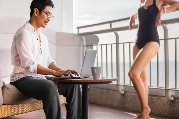 Succesvolle zakenman die op vakantie werkt achter een laptop met uitzicht op de oceaan