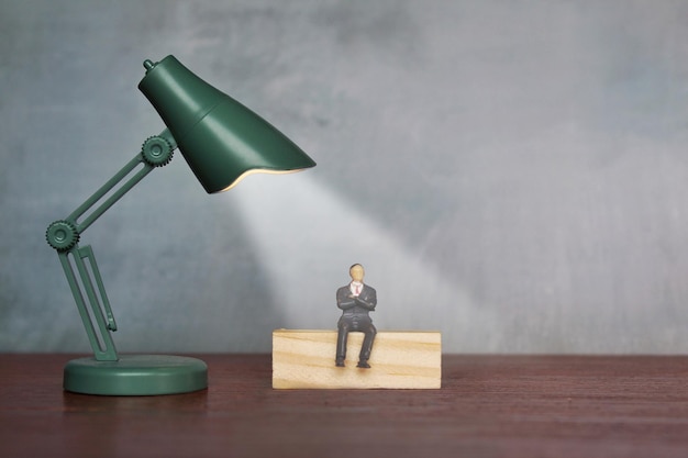 Succesvolle zakenman onder spotlight bedrijfsconcept Miniatuur man zit onder bureaulamp