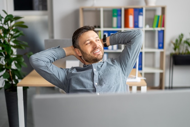 Succesvolle zakenman ontspannen volwassen man hand in hand achter hoofd zit aan bureau in moderne kantoren