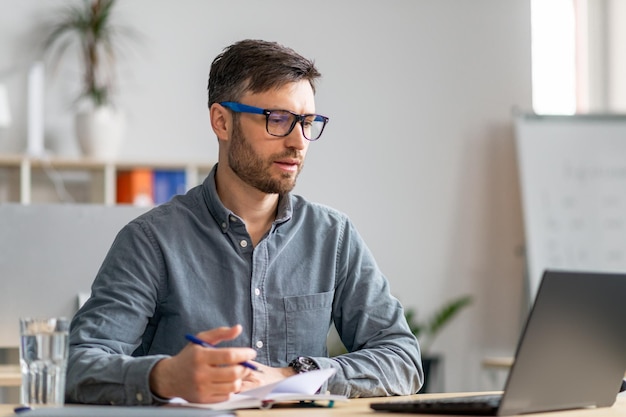 Succesvolle zakenman van middelbare leeftijd die op kantoor aan het werk zit voor een laptop en